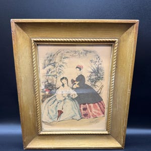May include: A framed print depicting two women in historical dresses, set in a garden. The print is in a gold-coloured wooden frame with a rope-like border. The women are in a garden setting with trees and foliage.