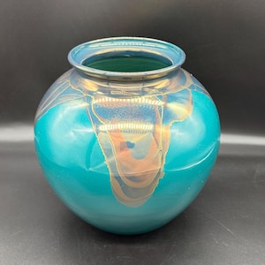 May include: A teal-colored, round vase with a wide opening. The vase has a glossy finish with gold and orange accents. The rim of the vase is a darker teal color. The vase is a decorative item.