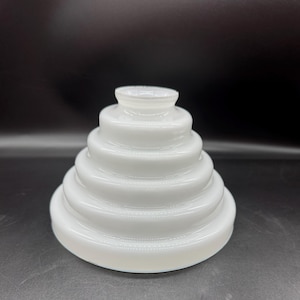 May include: A white milk glass light fixture shade featuring a stepped, tiered, conical silhouette. The glass has a smooth, glossy finish with five distinct concentric rings that decrease in diameter as they reach the top opening.