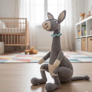 May include: A handmade gray crochet donkey toy with a long neck, floppy ears, and a light blue ruffled collar. The donkey is sitting on a wooden floor in a child's room. The toy has beige accents on its legs and face.