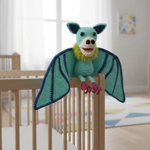 May include: A handmade crochet bat toy in teal, navy blue, yellow, and pink. The bat has large wings, a smiling face, and is perched on a wooden crib. The toy is designed with a soft, textured yarn.