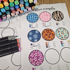 Könnte beinhalten: Eine Sammlung farbiger Kunstmarker und Musterbeispiele auf Papier. Das Papier zeigt verschiedene kreisförmige Designs mit Mustern wie Schneeflocken, Leopardenmuster und Blumenmotiven. Der Text "Pattern examples" ist sichtbar.