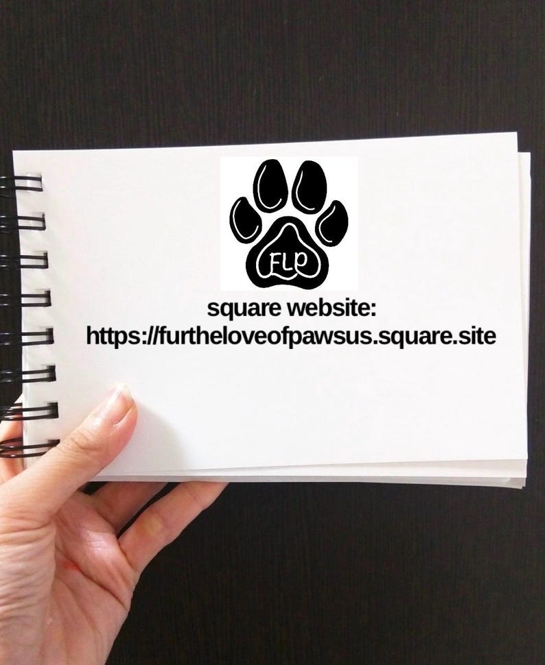 May include: A white notebook with a black paw print logo and the text "square website: https://furtheloveofpawsus.square.site" on the front.