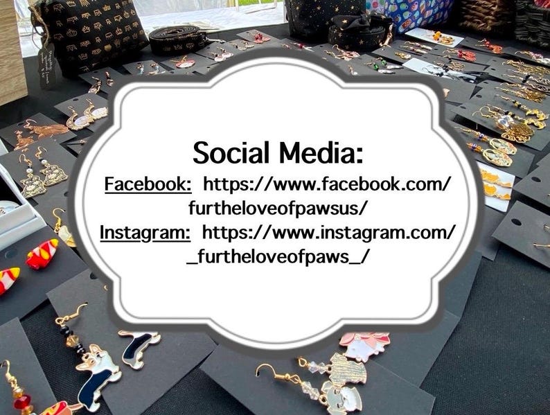 May include: A white sign with black text that reads "Social Media: Facebook: https://www.facebook.com/furtheloveofpawsus/ Instagram: https://www.instagram.com/_furtheloveofpaws_/". The sign is surrounded by a variety of colorful earrings.