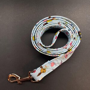 May include: A blue and white dog leash with a gold metal clip. The leash has a pattern of cartoon characters and flowers.
