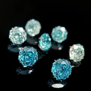 May include: A group of seven teal blue faceted glass gems on a black background. The gems are various sizes and shapes.