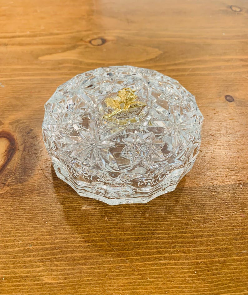 May include: A clear glass trinket box with a starburst pattern and a gold leaf design on the lid.
