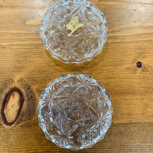 May include: Two clear glass trinket boxes with a starburst pattern. The top box has a gold rose design on the lid.