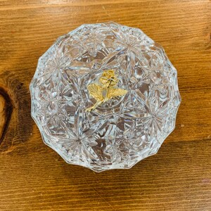 May include: A clear glass trinket box with a cut glass design and a gold rose accent.