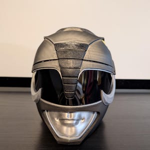 Op de afbeelding: Een zwarte en zilveren Power Rangers helm met een vizier en een gedetailleerd ontwerp.