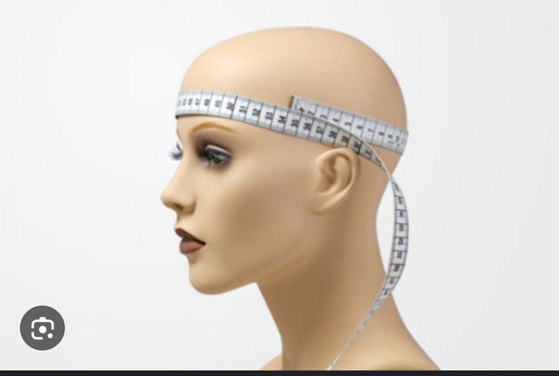 Puede incluir: Una cabeza de maniqu&iacute; con una cinta m&eacute;trica blanca envuelta alrededor de la cabeza. La cinta est&aacute; marcada en cent&iacute;metros. El maniqu&iacute; tiene un tono de piel neutro, con maquillaje aplicado en los ojos y los labios.