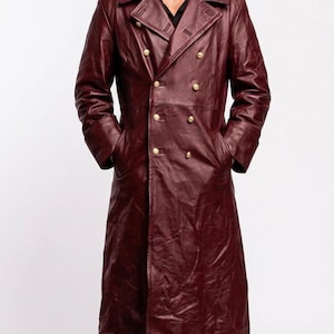 May include: A long, burgundy leather coat with a double-breasted design and gold-colored buttons. The coat has a wide collar and pockets. The person in the image is wearing black boots.
