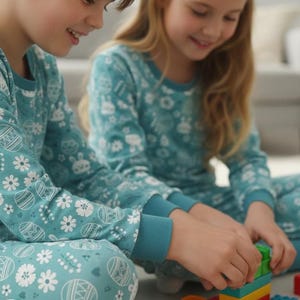May include: Two children wearing matching teal pajamas with an Easter-themed print of eggs, bunnies, and flowers. They are sitting on the floor and playing with colorful building blocks. The pajamas have long sleeves and a crew neck.