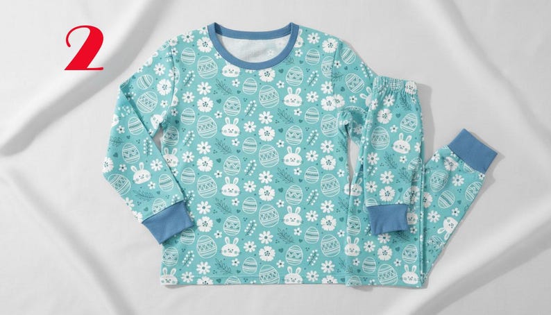 May include: A two-piece pajama set in a light teal color, featuring a repeating pattern of Easter eggs, bunnies, and flowers. The long-sleeved top and pants have blue cuffs and trim. The number "2" is in the top left corner.