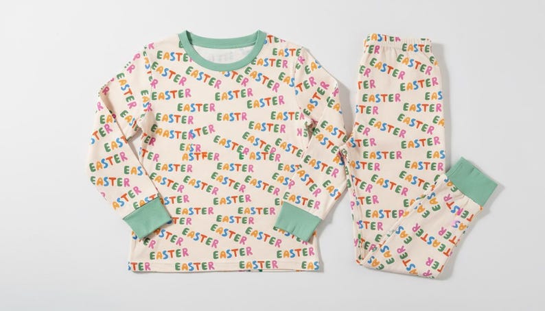 K&ouml;nnte beinhalten: Cremefarbenes Oster-Pyjama-Set mit einem lang&auml;rmligen Oberteil und einer Hose. Der Pyjama ist mit dem Wort "EASTER" in verschiedenen Farben bedeckt. Die B&uuml;ndchen und der Halsausschnitt sind mintgr&uuml;n.