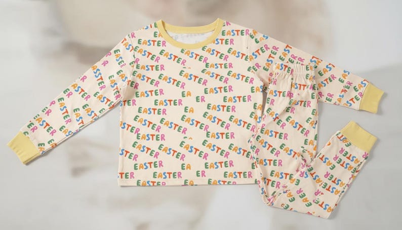 K&ouml;nnte beinhalten: Cremefarbenes Ostern-Pyjama-Set mit einem lang&auml;rmeligen Oberteil und einer Hose. Das Pyjama ist mit dem Wort "EASTER" in verschiedenen Farben bedruckt. Die B&uuml;ndchen und der Halsausschnitt sind gelb.