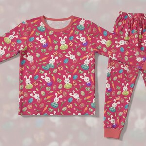 May include: A pink pajama set with a pattern of white bunnies, carrots, butterflies, and Easter eggs. The long-sleeved top and trousers have matching cuffs and a round neckline. The set is designed for comfort.