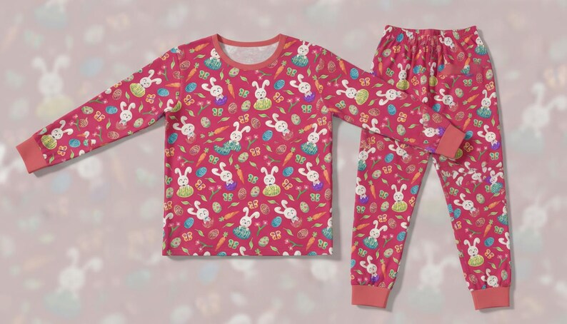 May include: A pink pajama set with a pattern of white bunnies, carrots, butterflies, and Easter eggs. The long-sleeved top and trousers have matching cuffs and a round neckline. The set is designed for comfort.