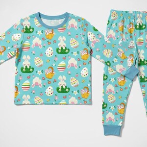 May include: A light blue pajama set featuring a repeating pattern of Easter eggs, bunnies, and baskets. The long-sleeved top and pants have blue cuffs and trim. The pajamas are designed for children.