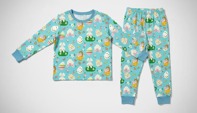 May include: A light blue pajama set featuring a repeating pattern of Easter eggs, bunnies, and baskets. The long-sleeved top and pants have blue cuffs and trim. The pajamas are designed for children.