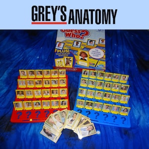 May include: A Grey's Anatomy themed Guess Who? board game. The game features two red and blue game boards with yellow character cards. The box reads "Guess Who?" and "Grey's Anatomy" in the top banner.