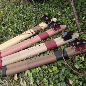 May include: Four cylindrical wooden flutes with finger holes, each featuring a distinct animal-shaped block attached to the top. The flutes vary in colour from light tan to dark brown, with decorative bands in red, black, and brown, and thin leather cords.