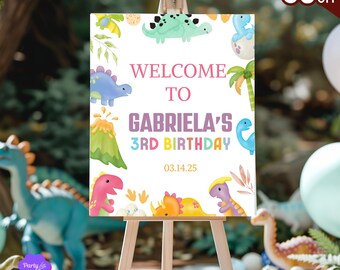 May include: A welcome sign for a 3rd birthday party with a dinosaur theme. The sign is white with colorful dinosaurs and a volcano. The text on the sign reads "Welcome to Gabriela's 3rd Birthday 03.14.25".