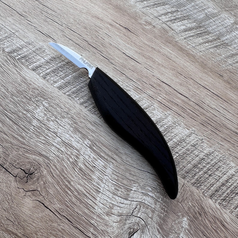 以下が含まれることがあります： 黒い柄と銀色の刃が付いた木彫りナイフ。柄は曲線的で人間工学に基づいています。刃は鋭く尖っており、詳細な彫刻作業に適しています。このナイフは、木工プロジェクトでの精度と制御のために設計されています。