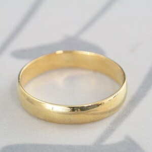 May include: A simple gold wedding band with a smooth, rounded surface.