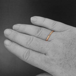 May include: A close-up of a hand wearing a thin, rose gold band with a textured design.