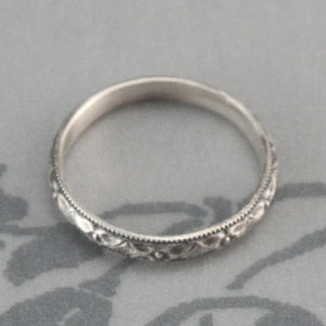 May include: A silver band ring with a delicate floral design.