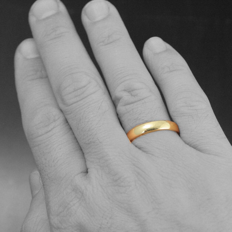 May include: A simple gold wedding band on a person's finger.