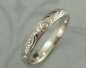 May include: A simple silver wedding band with a delicate engraved floral design.