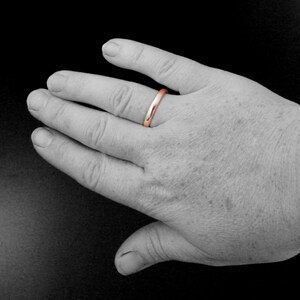 May include: A simple, polished, silver wedding band with a rose gold interior.