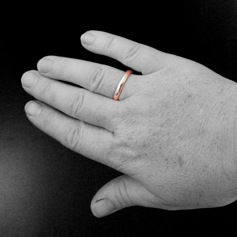 May include: A simple, polished, silver wedding band with a rose gold interior.