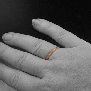 May include: A simple, thin, gold band ring worn on a finger.