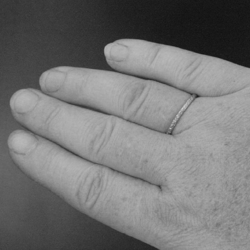 May include: A close-up of a hand wearing a thin silver band ring.