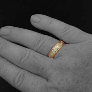 以下が含まれることがあります： 繊細な渦巻き模様が施された金の結婚指輪。指につけられています。
