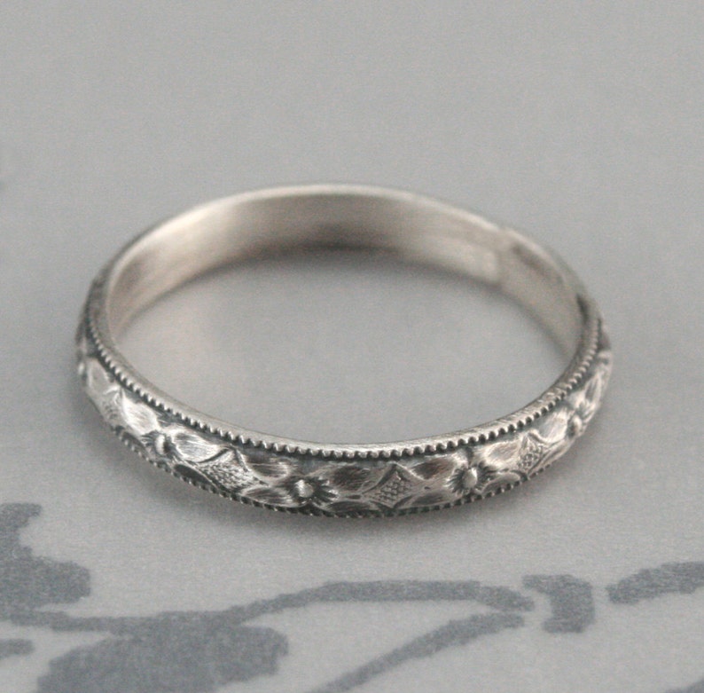 May include: A silver band ring with a delicate floral design. The ring is thin and has a smooth, polished finish.