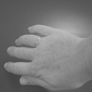 Puede incluir: Primer plano de una mano con un fino anillo de banda de plata en el dedo anular.