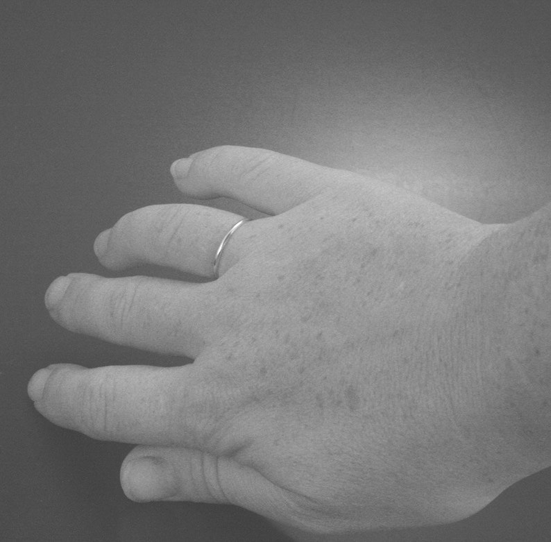 Puede incluir: Primer plano de una mano con un fino anillo de banda de plata en el dedo anular.