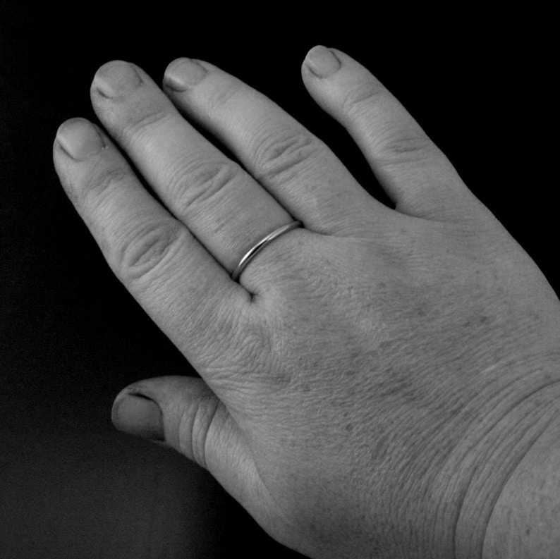 Puede incluir: Primer plano de una mano con un fino anillo de banda plateada en el dedo anular.