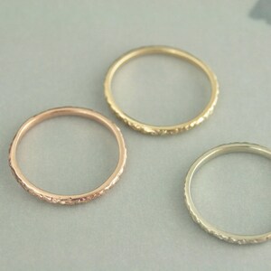 May include: Three simple gold bands with a textured edge. The bands are in rose gold, yellow gold, and white gold.