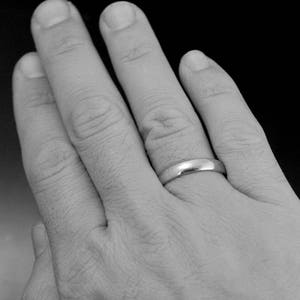May include: A close-up of a hand wearing a simple silver wedding band.