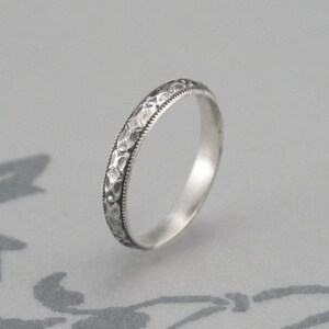 May include: A silver band ring with a delicate floral design engraved around the entire band.