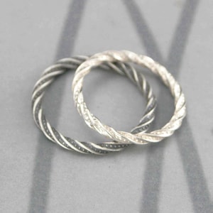 May include: Two silver-colored rings with a twisted rope design. The rings are circular and appear to be made of metal. The rings are displayed on a gray surface.