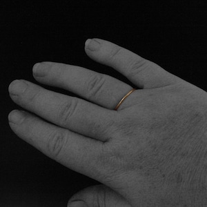 May include: A simple gold band ring worn on a person's finger.