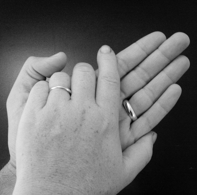 May include: Two hands with wedding bands on their ring fingers, intertwined together. The hands are in a close-up view, with the background blurred.