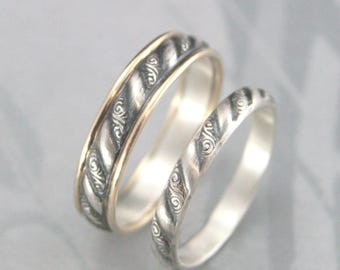 May include: Two silver rings with a twisted rope design and ornate detailing. One ring has a gold band. The rings are likely wedding bands or promise rings. The rings are displayed on a light gray background.