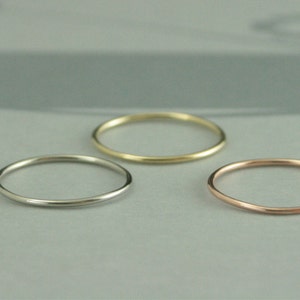 May include: Three thin metal rings in different colors: silver, gold, and rose gold. The rings are stacked on top of each other.